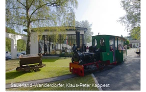 Menschen sitzen in einer fahrenden grünen Lok auf dem Museumsgelände