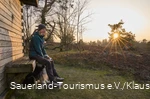 Auf einer Bank an einer Hütte auf dem Kahlen Pön sitzt Frau mit Hund im Winterlicht